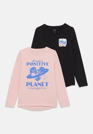 Due magliette a maniche lunghe: una rosa con testo e grafica blu, e una nera con un messaggio stampato colorato. Entrambe sono fatte di cotone morbido.