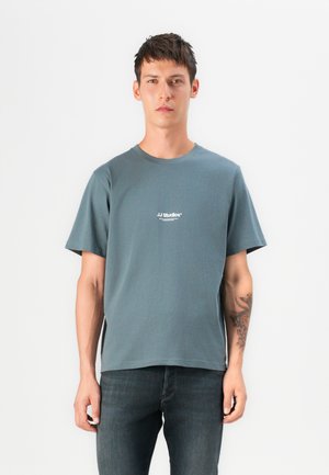 Gray cotton T-shirt with a crew neck, short sleeves, and side slits. Features white printed logo on the chest. Worn with dark denim jeans.
