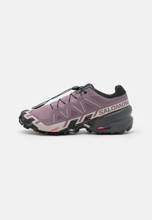 Chaussure de trail running Salomon violette et noire avec semelle noire robuste et système de laçage rapide sur fond blanc uni.
