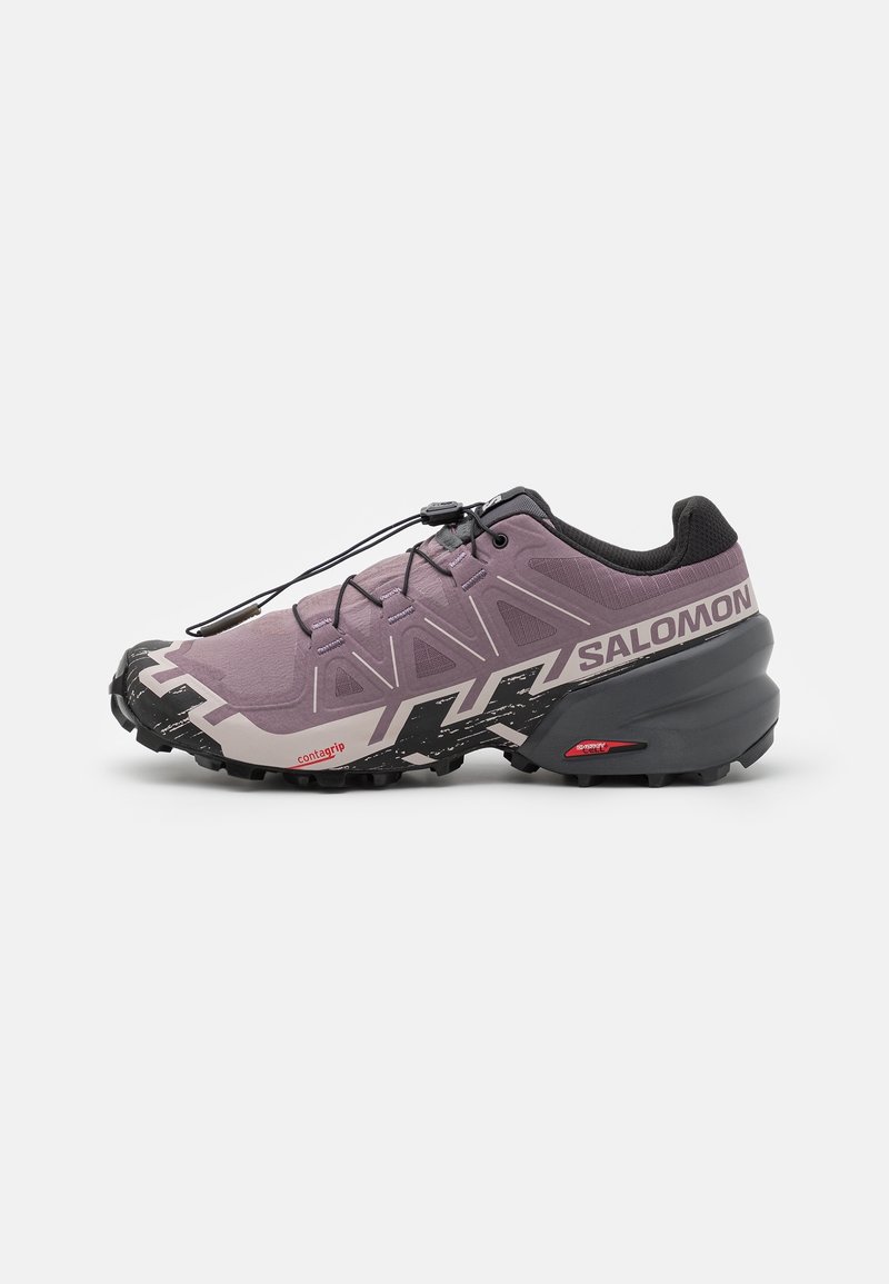 Chaussure de trail running Salomon violette et noire avec semelle noire robuste et système de laçage rapide sur fond blanc uni.