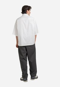 White short-sleeve shirt with a back yoke, paired with dark gray loose-fit trousers and black and white sneakers. Standard fabric texture.