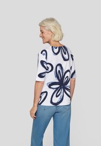White short-sleeve shirt with navy blue floral pattern, featuring large abstract shapes. Paired with light blue wide-leg jeans.