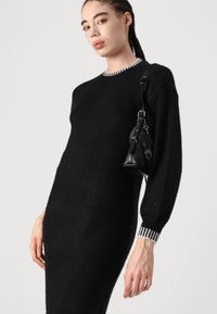 Crna pletiva haljina s dugim rukavima i rebrastim ovratnikom. Ima bijele prugaste detalje na manžetama. Nosena je mala crna torbica.