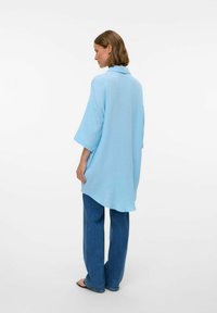 Light blue oversized shirt made of textured fabric with a collar and wide sleeves, paired with blue wide-leg jeans.