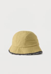 Ανοιχτό καφέ καπέλο τύπου καμπάνα με μαύρο περίγραμμα, διακοσμημένο με επαναλαμβανόμενο λευκό κείμενο "THE NORTH FACE" σε λευκό φόντο.