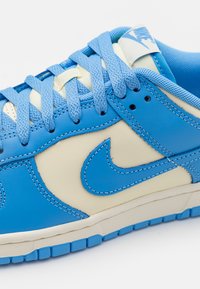 Plave i kremaste kožne tenisice s teksturiranim vezicama, prepoznatljivim swoosh logom i gumenom potplatom s uzorkom. 