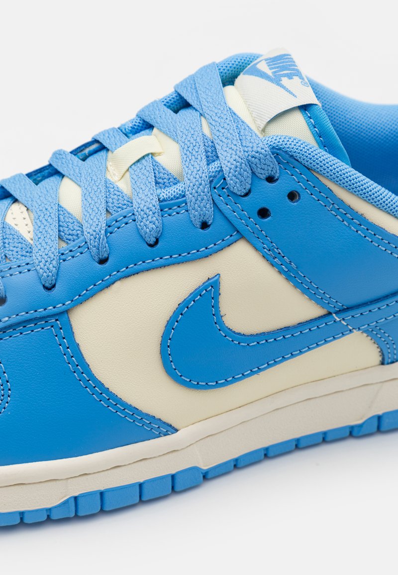 Zapatillas de piel azul y crema con cordones texturizados, un distintivo logo de swoosh y una suela de goma con un dibujo en relieve.