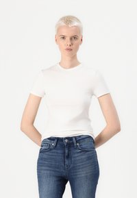 Hvit kortermet t-skjorte i bomull, rund hals, tettsittende fasong, kombinert med høyhårede blå jeans med en lett falming.