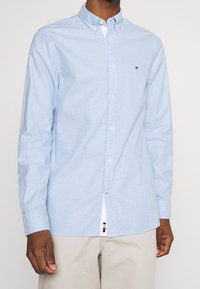 Lichtblauw overhemd van katoen met een brede kraag, lange mouwen en een klein logo op de borst.