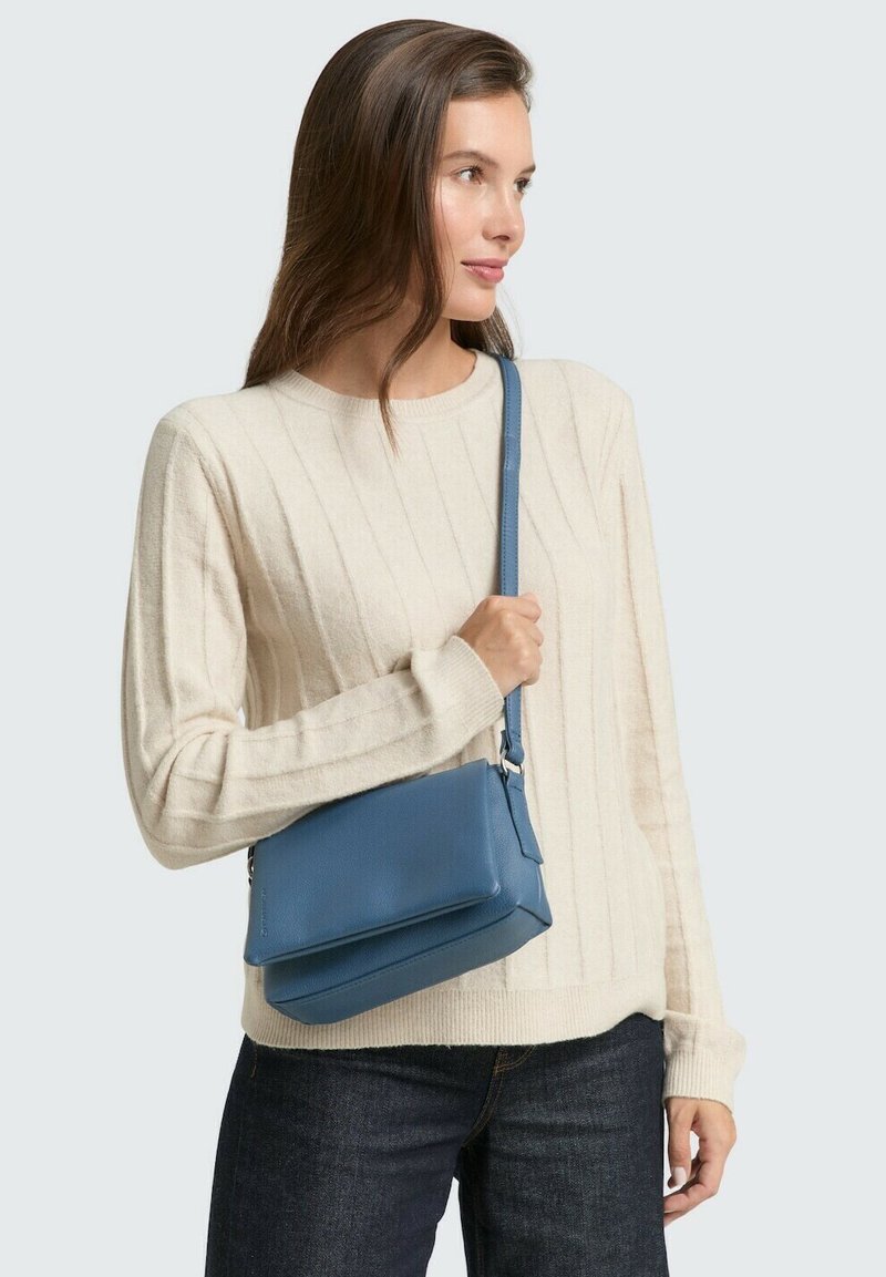 Maglione a coste di un beige chiaro con maniche lunghe, abbinato a una piccola borsa a tracolla in pelle blu di forma rettangolare e con tracolla regolabile.