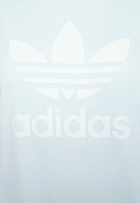 Ljusblå bomulls-t-shirt med en stor vit Adidas-logotyp med tre ränder och en treklöverdesign på framsidan.