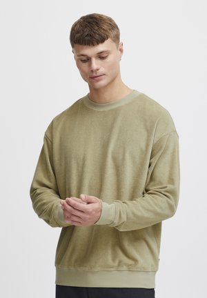 Olíva zöld pulóver puha, struktúrált anyagból. Kerek nyakkivágással, ejtett vállakkal, valamint bordázott mandzsettákkal és szegéllyel rendelkezik. Laid-back fazon.