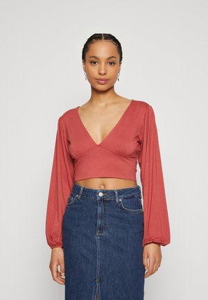 Kobberfarget, kort topp med dyp V-hals og lange puffermer, kombinert med en denim blyantnederdel med frontslitt og knappelukking.