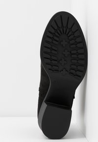 Czarne zamszowe buty z teksturowaną gumową podeszwą o wzorzystym bieżniku. Obcas jest solidny i lekko podwyższony.