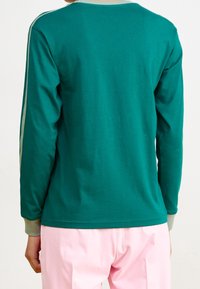 Person som bär en turkos långärmad skjorta med vita ränder på ärmarna och ljusrosa byxor, sedd från ryggen.