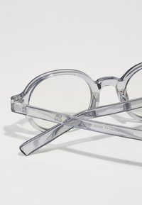Clear oval sunglasses with transparent frames. Features include a wide bridge, slim temples, and light gray lenses. Minimalist design with no noticeable hardware.