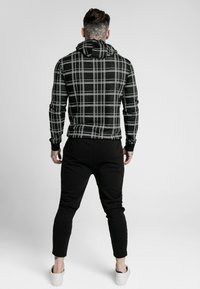 Black and white plaid hooded sweatshirt with long sleeves, paired with black slim-fit joggers and white slip-on shoes.