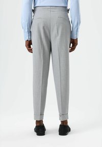 Pantalon gris avec un motif texturé, coupe ajustée, poches latérales et ourlets retroussés, associé à des chaussures noires et une chemise bleu clair.