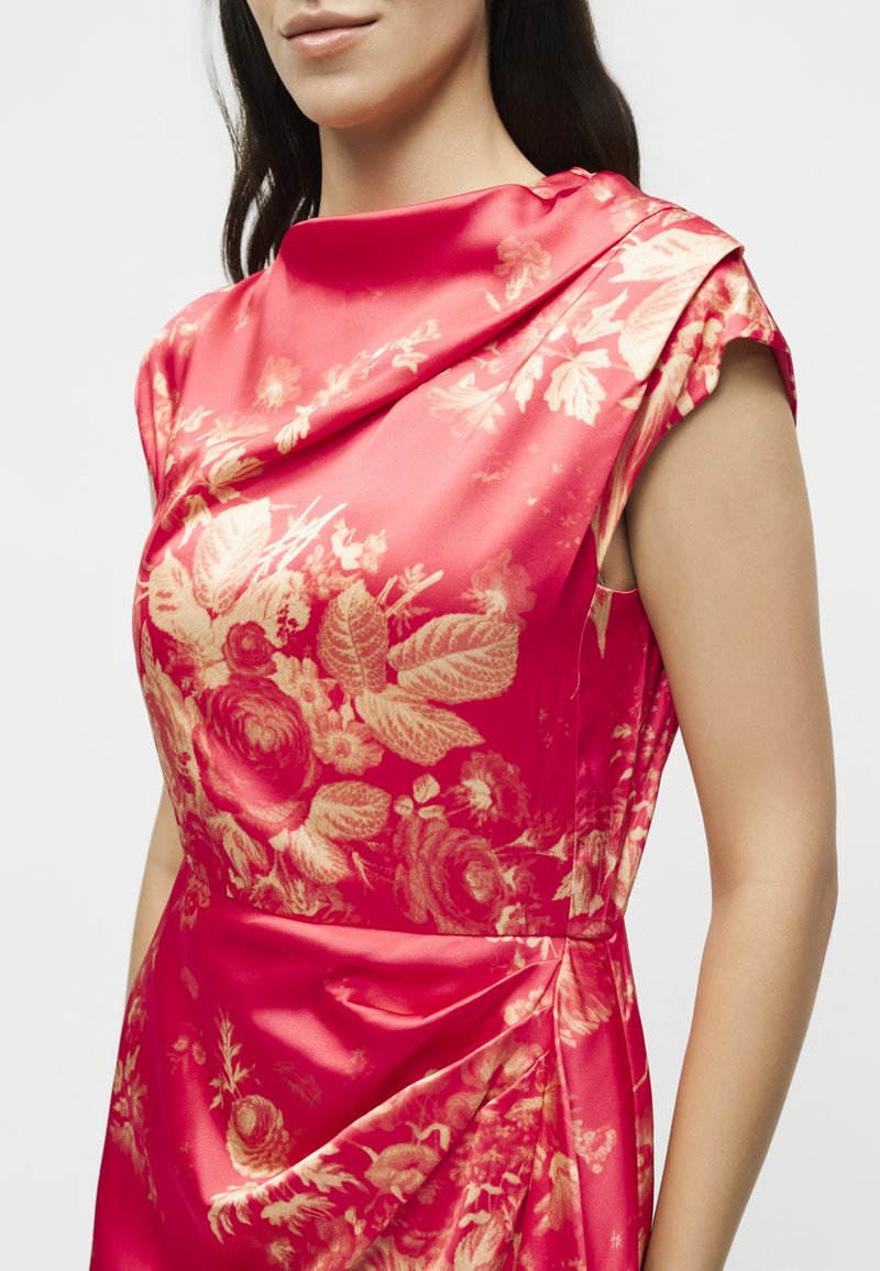 Donna che indossa un vestito rosa brillante senza maniche con motivi floreali dorati e scollo drappeggiato, visibile dalle spalle alla vita.