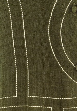 Groene stof met witte stikpatronen die lijnen en krommingen vormen. De textuur lijkt glad met een subtiele glans. Knopdetail zichtbaar.