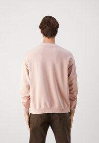 Sudadera de cuello redondo en color rosa claro con puños y dobladillo acanalados, hecha de una tela suave. La vista trasera muestra un diseño sencillo y liso, sin patrones.