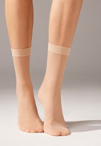 Calcetines tobilleros nudosos hechos de tela translúcida, con una suave banda elástica en el puño y una textura lisa y ligeramente brillante.