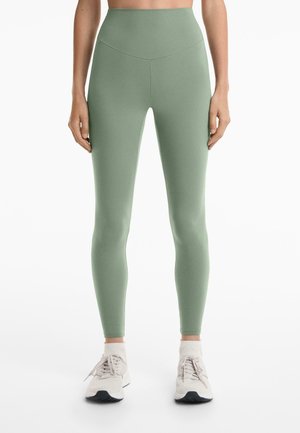 Light green high-waisted leggings made from stretchy fabric, featuring a smooth texture and form-fitting design. Paired with light sneakers.
