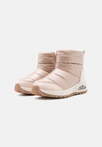 Botines de tobillo de color beige claro que presentan un diseño acolchado, textura suave y una suela intermedia blanca con una unidad de aire visible en el talón.
