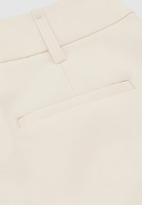 Záber zblízka na béžové látkové nohavice zobrazujúce zadný vrecko a slučku na opasok s viditeľnými detailmi šitia.