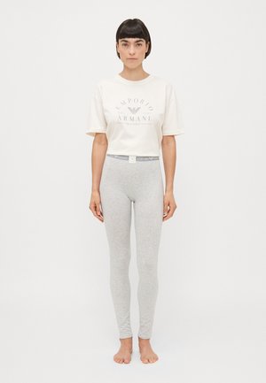 Balta īsā T-kreklā ar pelēku Emporio Armani grafiku, apvienota ar gaismas pelēkām legingām ar pieguļošu dizainu un logotipa jostu.