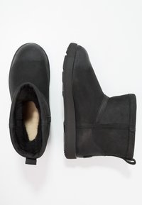 Czarne botki za kostkę z gładką skórzaną powierzchnią, okrągłym noskiem, podszyciem z polaru oraz gumową podeszwą. Wyposażone w pętelkę ułatwiającą zakładanie.