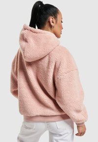 Roze fleece hoodie met een gestructureerde afwerking, oversized pasvorm en een trekkoordkap. De manchetten en de zoom hebben een glad ribbelontwerp.