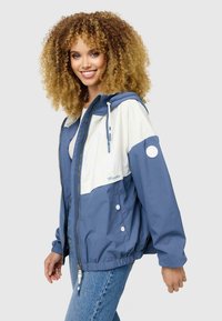Veste coupe-vent avec un design bicolore en bleu et blanc, avec fermeture éclair à l'avant, capuche ajustable et taille élastique. Texture lisse.
