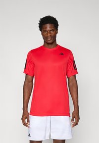 Camiseta deportiva roja de manga corta con acentos de logo negros. Textura suave, escote redondo y diseño ligero adecuado para actividades deportivas.
