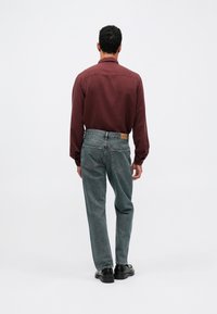 Bordo garās piedurknes krekls un izbalējuši zili džinsi. Krekla piedurknes ir ar pogām, džinsiem ir kabatas un ādas uzlīme aizmugures jostas vietā.