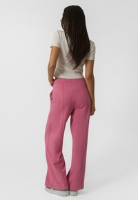 Pantalons larges roses avec une texture lisse, poches latérales et couture détaillée ; associés à un haut ajusté de couleur claire.