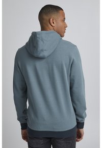 Sudadera con capucha de suave tejido gris azulado, con un corte relajado, puños y dobladillo de canalé. Los detalles incluyen una superficie texturizada y capucha.
