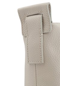 Angolo di una borsa in pelle beige con finitura testurizzata, dotata di una patta piegata e dettagli di cucitura visibili lungo il bordo.