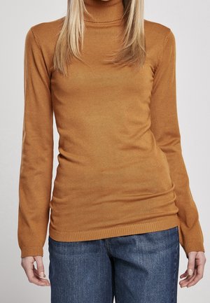 Personne portant un pull à col roulé marron près du corps et un jean en denim bleu, debout les bras détendus le long du corps sur un fond uni.