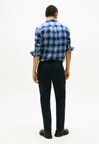 Camicetta a scacchi blu con maniche arrotolate, abbinata a pantaloni cargo navy con tasche laterali e texture liscia, vista da dietro.