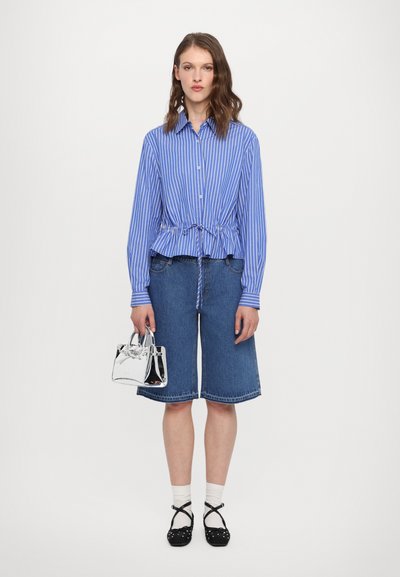 Blå- och vitrandig skjorta med knappar och insnitten midja, matchad med denim culotter. Bär en liten silverfärgad handväska och har på sig svarta ballerinaskor.