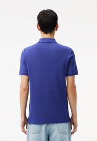 Camisa polo azul hecha de tejido texturizado, con un cuello clásico y mangas cortas. La vista trasera muestra un corte recto y sin adornos.