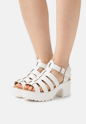 Witte platform sandalen met brede kruisbanden, een gespsluiting en een gestructureerde rubberen zool met groeven voor grip.