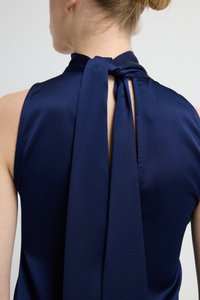 Tmavě modrý tílko bez rukávů s vysokým límcem a zavazováním vzadu, s malým průstřihem ve tvaru klíčové dírky. Hladká, lesklá textura látky.