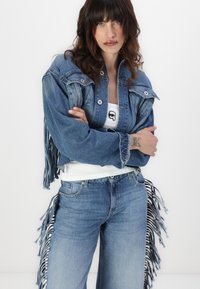 Denimjack met franjes, in een lichtblauwe kleur en met een cropped ontwerp. Gecombineerd met bijpassende denim jeans, die beide een gestructureerde afwerking hebben.