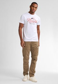 Camiseta blanca de algodón con un gráfico rojo que dice "Petrol Ind Miami U.S.A." combinada con pantalones cargo beis y zapatillas blancas.
