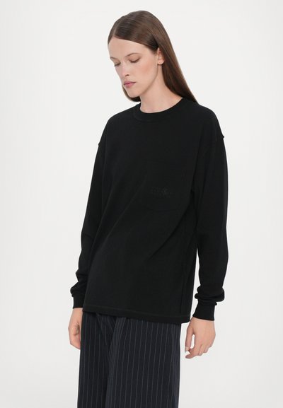Svart långärmad t-shirt med rund halsringning och bröstficka. Mjuk tygkvalitet med avslappnad passform och subtila sömdetaljer.