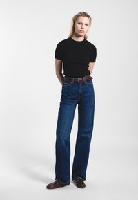 Black fitted t-shirt, unembellished, paired with high-waisted, straight-leg blue jeans. Brown leather belt accents the waist. Brown shoes included.
