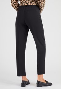 Zwarte op maat gemaakte broek met een slim fit ontwerp, voorzien van twee achterzakken. Draagt met zwarte mocassins. Glad stofmateriaal.