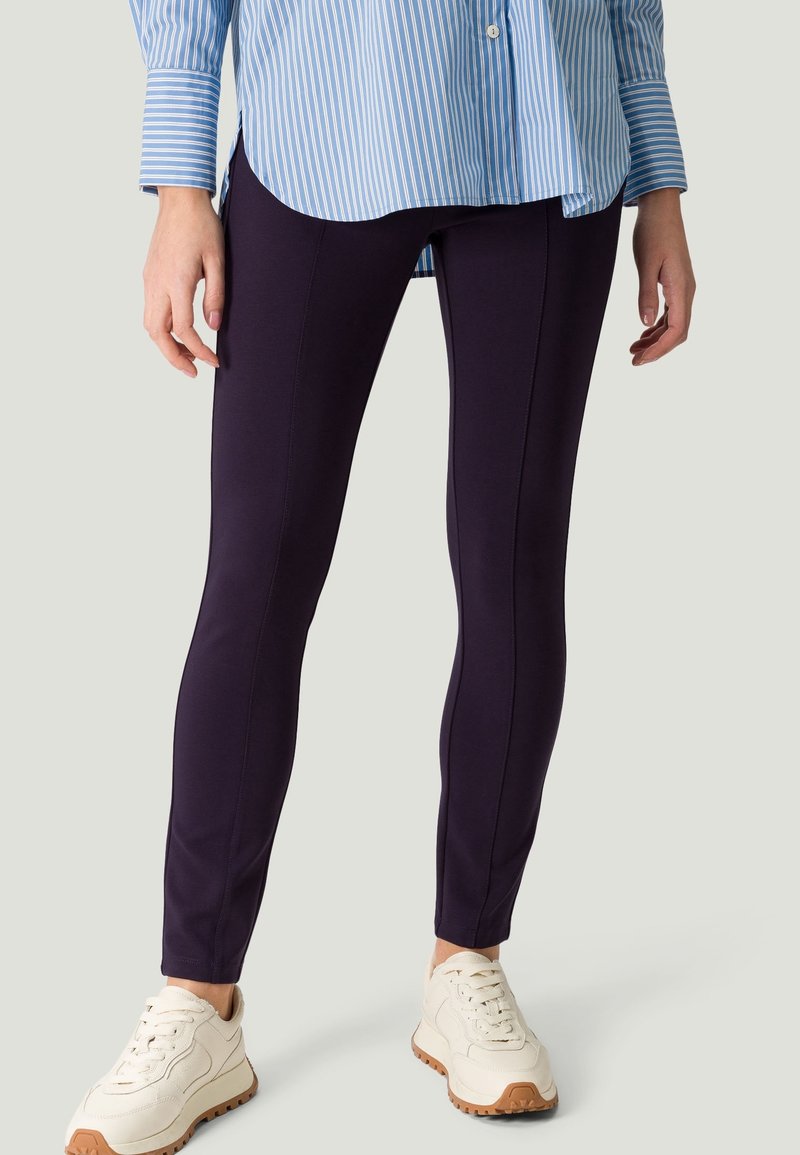 Leggings blu navy con una texture liscia, caratterizzati da cuciture frontali e una vestibilità aderente, abbinati a una camicia a righe blu chiaro e sneakers bianche.